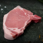 Schweinekotelett vom Strohschwein, fachgerecht pariert mit Knochen auf Schiefer präsentiert für Gezer Gastronomie-Kunden.