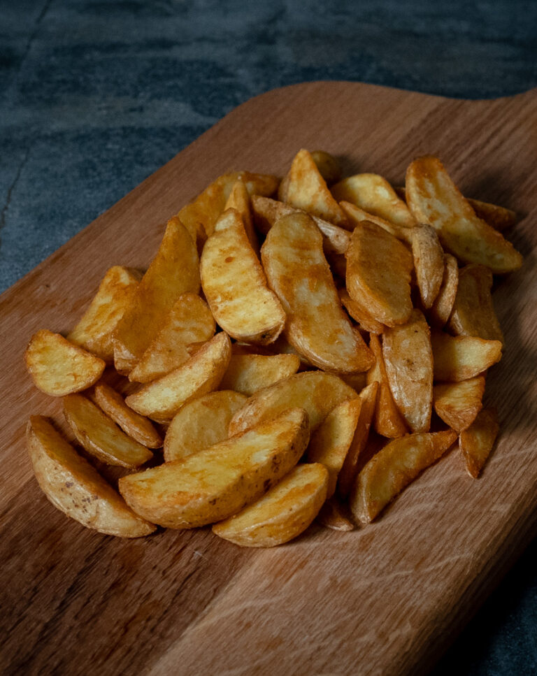 Knusprig frittierte, goldbraun gewürzte Aviko Wedges mit Schale auf einer holzernen Servierplatte, präsentiert für Gezer-Kunden